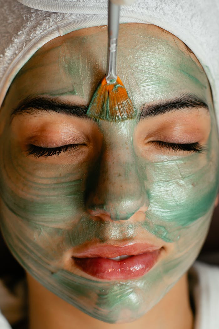hero-img-02 Close-up of a woman enjoying a green cosmetic facial mask application at a spa.