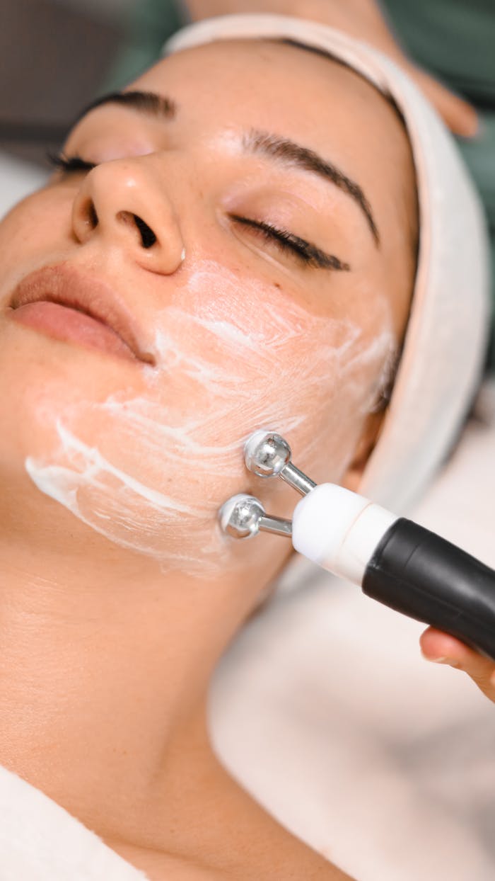 gallery-5 Close-up of a woman getting a facial treatment with a massager and face cream in a spa setting.