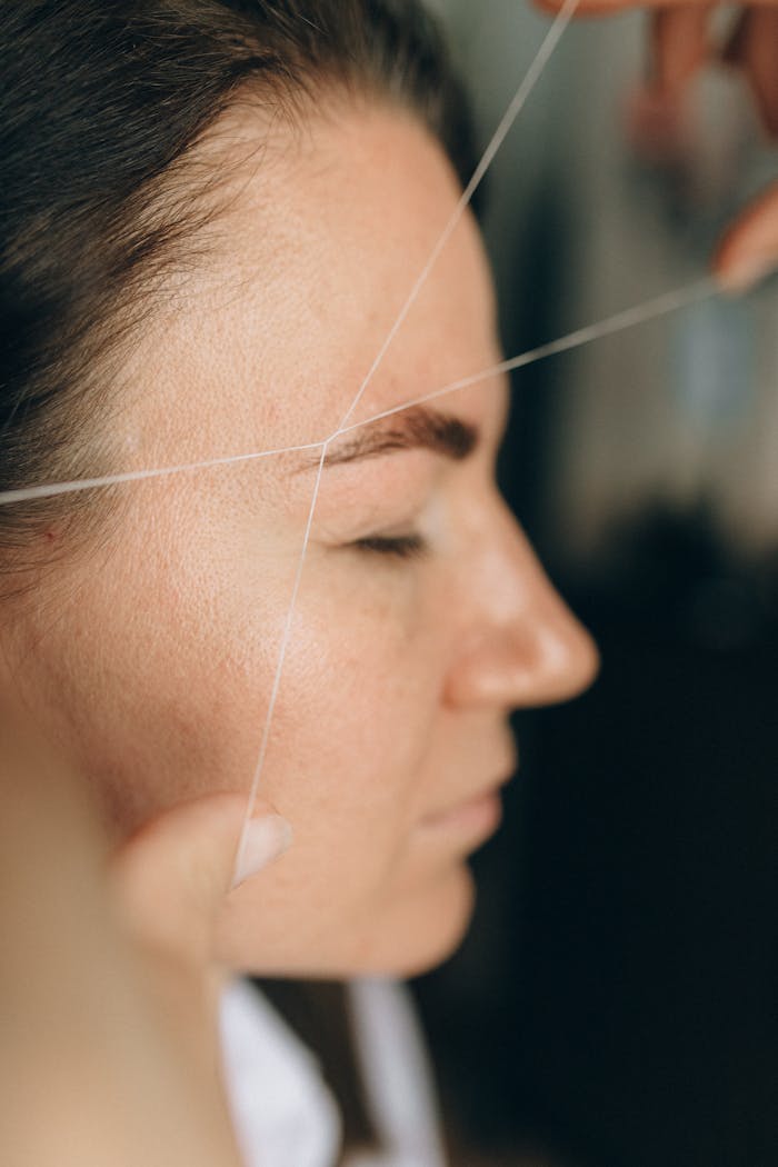 about-01 Side view of a woman receiving eyebrow threading at a salon.